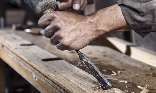 43569456 - hands of carpenter with chisel in the hands on the workbench in carpentry